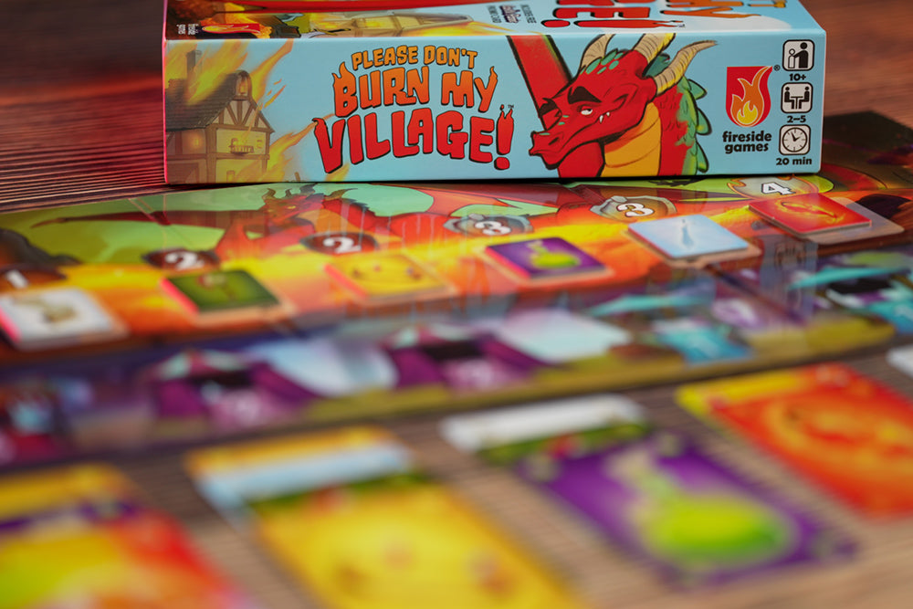 The board from Please Don't Burn My Village in the foreground, blurry, with the box behind it in focus.