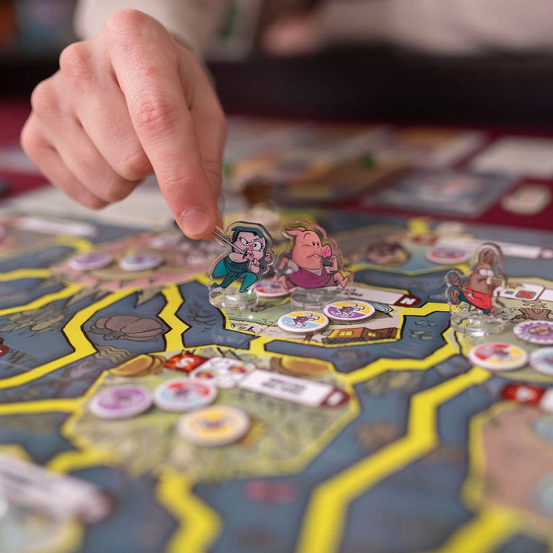 Board game with character figures of Ronin, Ham, and Malcom, plus colorful tiles, a hand interacting with the figures.