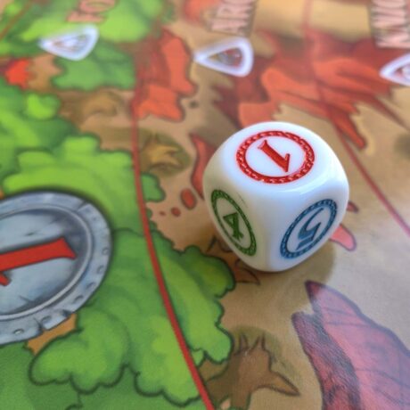 A close up of a white six-sided die with red, blue and green numbers sitting on a colorful game board