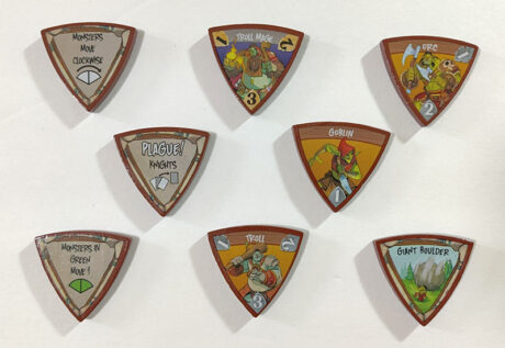 Triangular wooden tokens with monster artwork on a white background