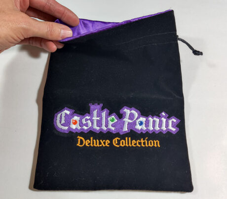 Black fabric bag with purple satin inside. "Castle Panic Deluxe Collection" embroidered on the front