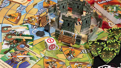 close up of the Castle Panic game board with dice, and cardboard tokens of the castle walls and towers, surrounded by monsters