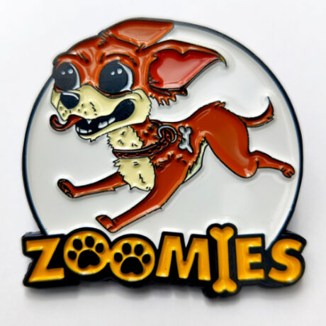 An enamel pin of a sprinting brown and cream cartoon chihuahua with the text Zoomies across the bottom.